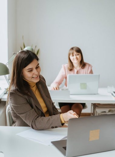 Two women working together with laptops in a bright and modern office setting.